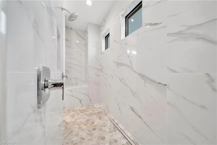 Walk-in shower with large format wall tiling, pebble-finish flooring, built-in bench, and polished chrome fixtures