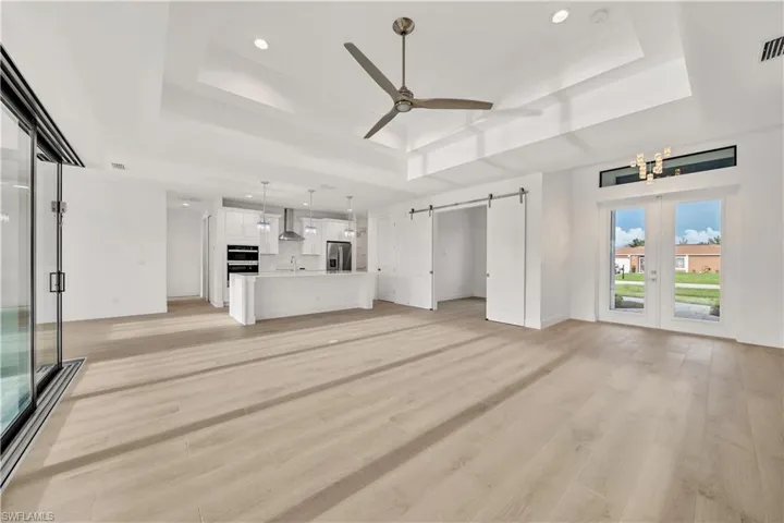 Spacious open-concept interior with light wood-finish flooring, a tray ceiling, and recessed lighting