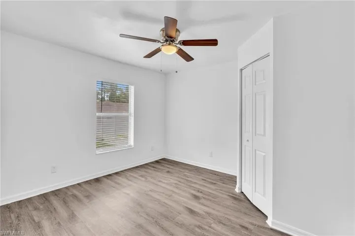 Neutral interior space featuring wood-finish flooring and a bright window with horizontal blinds