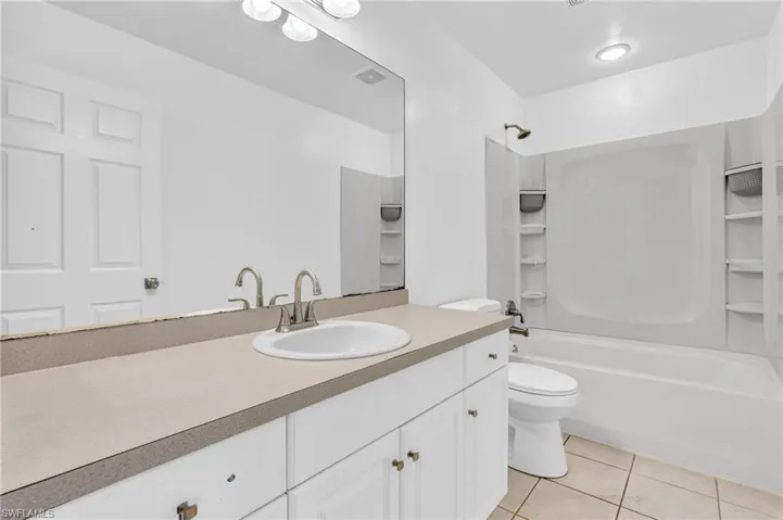Bathroom featuring a single vanity with an integrated sink, broad wall mirror, and a white bathtub with a shower combination