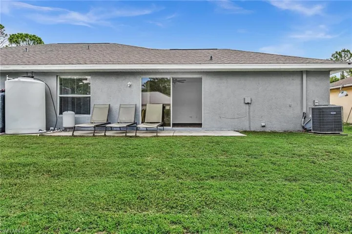 Expansive backyard featuring a concrete patio, sliding glass doors, and a large water storage tank