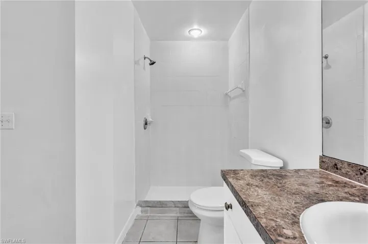 Bathroom featuring a tiled shower stall with a built-in shelf, a toilet, and a vanity with a dark patterned countertop and an integrated sink