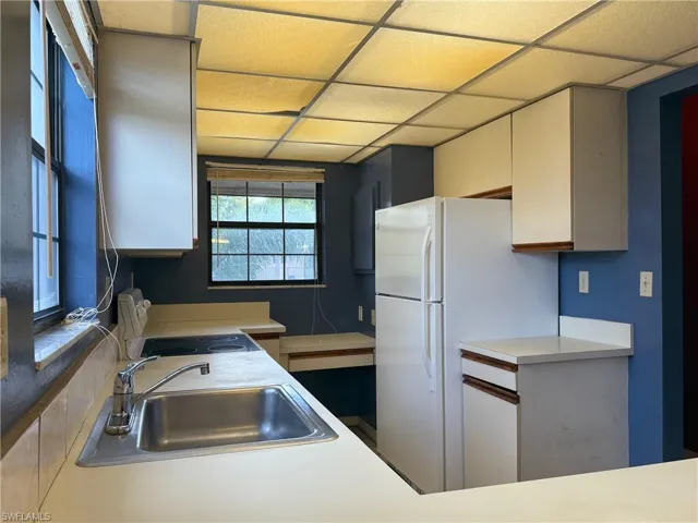 Kitchen featuring freestanding refrigerator, electric stove, light countertops, a drop ceiling, and white cabinetry