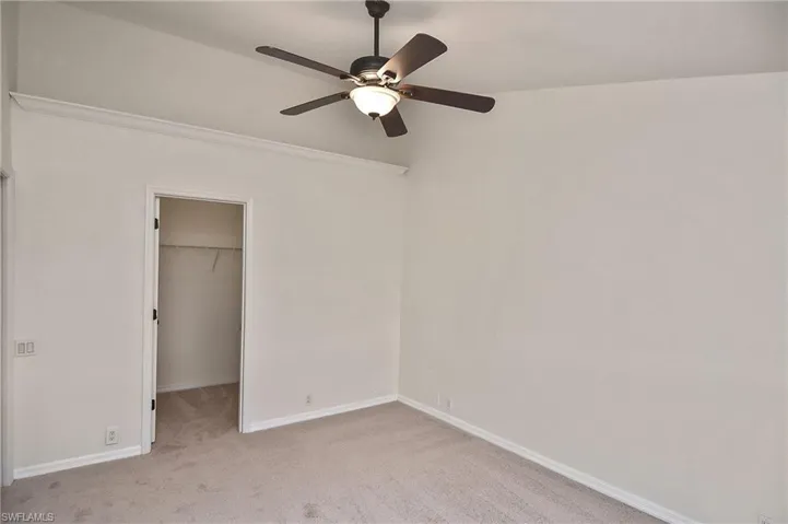 Unfurnished bedroom with light carpet, ceiling fan, a walk in closet, and a closet