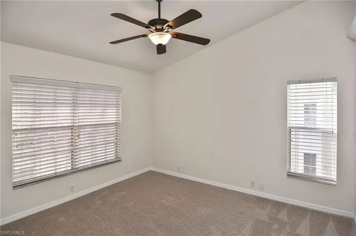 Carpeted empty room featuring ceiling fan and lofted ceiling