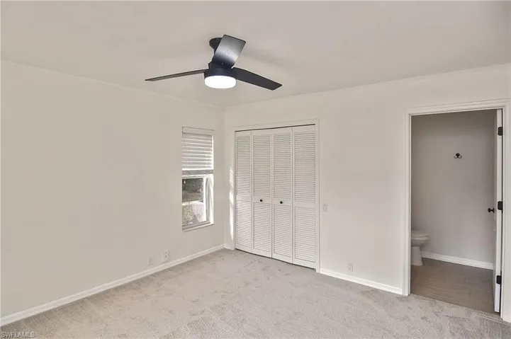 Unfurnished bedroom with ensuite bathroom, ceiling fan, a closet, and light colored carpet