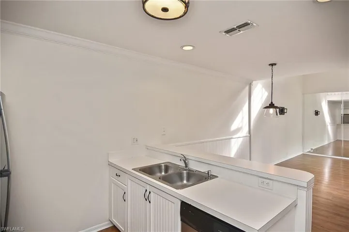 Kitchen with white cabinets, black dishwasher, hanging light fixtures, hardwood / wood-style flooring, and sink