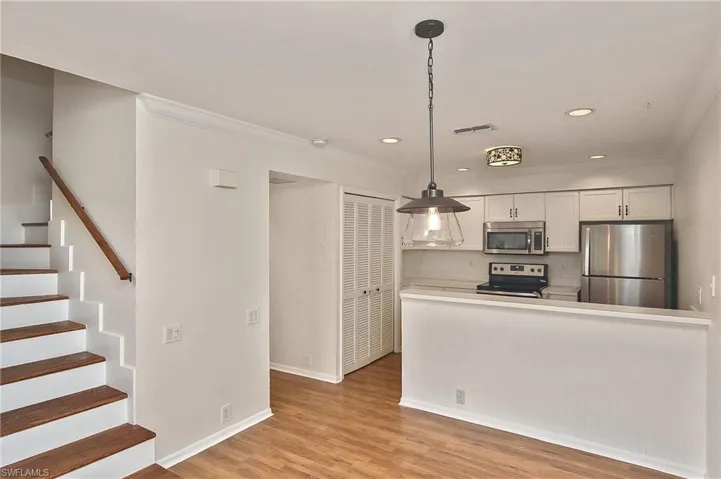 Kitchen featuring crown molding, stainless steel appliances, light wood-type flooring, hanging light fixtures, and white cabinets