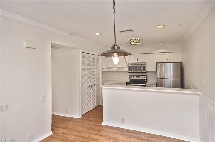Kitchen with light hardwood / wood-style floors, white cabinetry, appliances with stainless steel finishes, ornamental molding, and hanging light fixtures