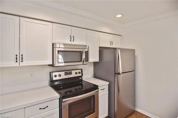 Kitchen with stainless steel appliances, hardwood / wood-style flooring, white cabinets, and ornamental molding