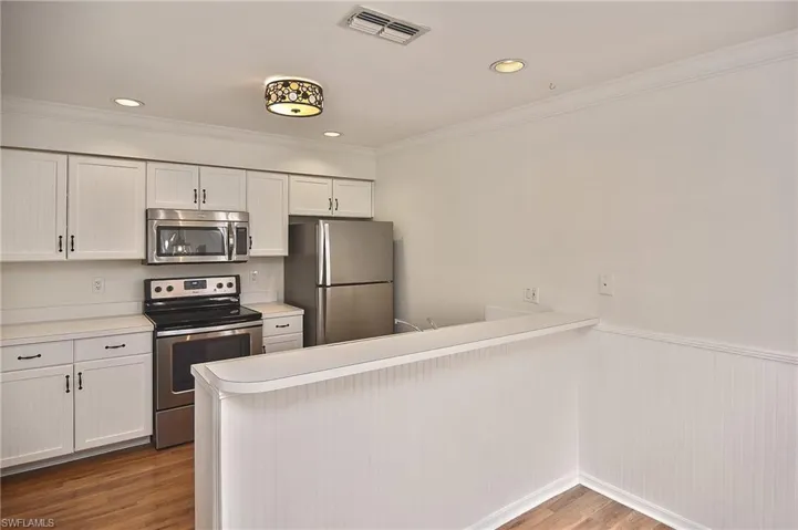 Kitchen featuring wood-type flooring, white cabinets, kitchen peninsula, ornamental molding, and appliances with stainless steel finishes