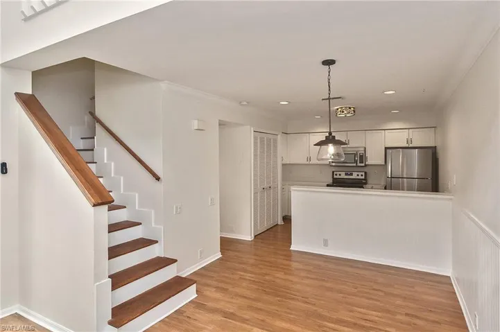 Kitchen with stainless steel appliances, light hardwood / wood-style floors, ornamental molding, hanging light fixtures, and white cabinets