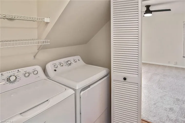 Laundry room featuring ceiling fan, light colored carpet, and washer and clothes dryer