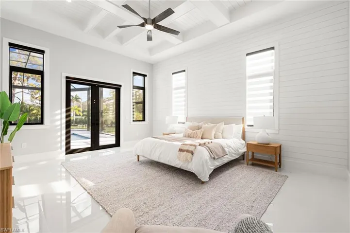 The luxurious primary suite offers direct access to the pool deck and a spa-like bathroom adorned in marbled tile, complete with dual vanities, an oversized shower, and a freestanding soaking tub
