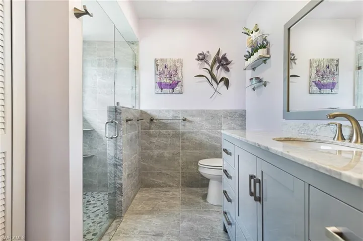 Bathroom featuring tile walls, toilet, tile patterned floors, vanity, and a shower with shower door