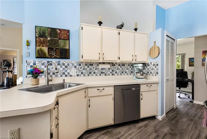 Kitchen featuring dark hardwood / wood-style floors, a towering ceiling, stainless steel dishwasher, tasteful backsplash, and sink