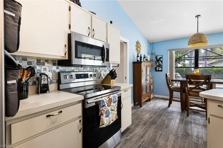 Kitchen with appliances with stainless steel finishes, lofted ceiling, backsplash, dark wood-type flooring, and decorative light fixtures