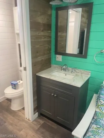 Half bath with wood walls, wood finished floors, and toilet