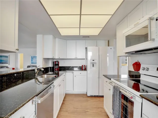 Kitchen with white appliances, white cabinetry, light wood-style flooring, and dark stone countertops