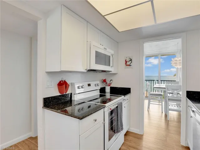 Kitchen with white appliances, light wood-type flooring, white cabinets, dark stone counters, and expansive windows
