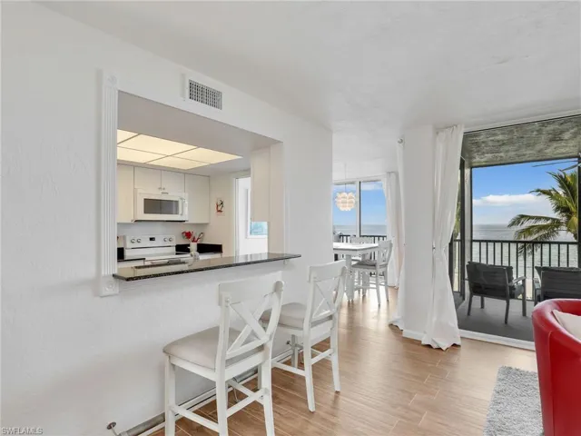 Kitchen featuring white appliances, light wood-type flooring, a breakfast bar area, dark countertops, and a water view