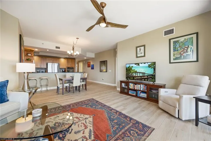 Living room with open floor plan featuring wood-like tiled floors and a ceiling fan looking towards kitchen.