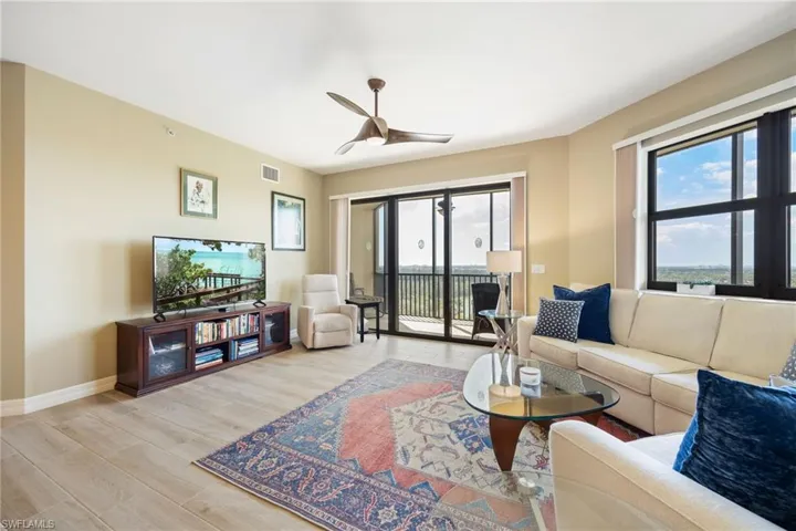 Living room with open floor plan featuring wood-like tiled floors and a ceiling fan.