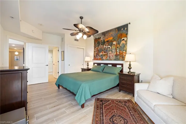 Primary Bedroom featuring wood-like tile floors, 2 closets, a sitting area and ceiling fan.