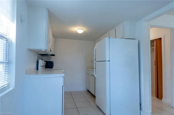 Kitchen with light tile patterned flooring, stove, white fridge, and white cabinets