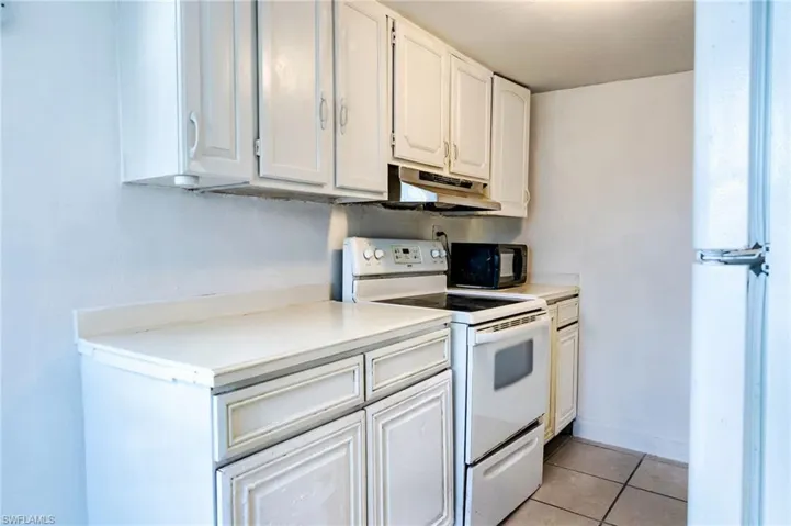 Kitchen featuring white cabinetry, light tile patterned floors, and white appliances