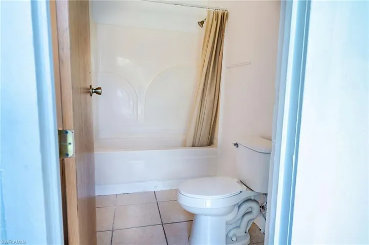 Bathroom featuring shower / bathtub combination with curtain, tile patterned floors, and toilet