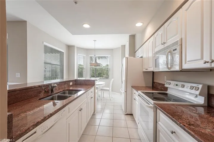 Kitchen with hanging light fixtures, dark stone countertops, white cabinets, white appliances, and sink