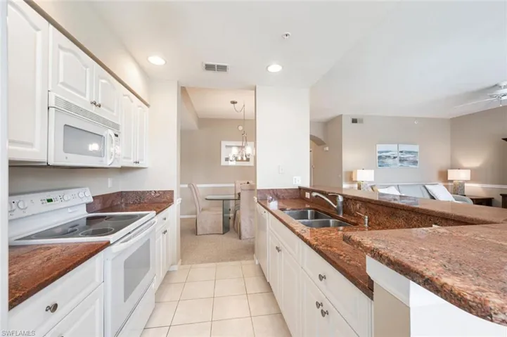 Kitchen featuring pendant lighting, dark stone counters, sink, white cabinetry, and white appliances