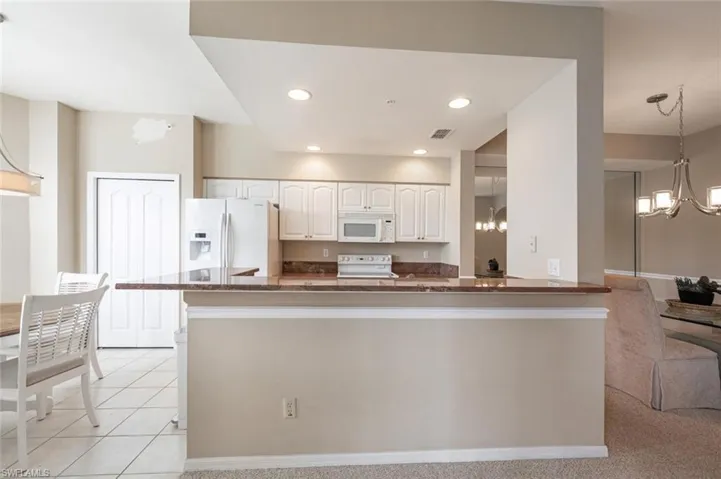 Kitchen featuring white cabinetry, white appliances, kitchen peninsula, pendant lighting, and light colored carpet