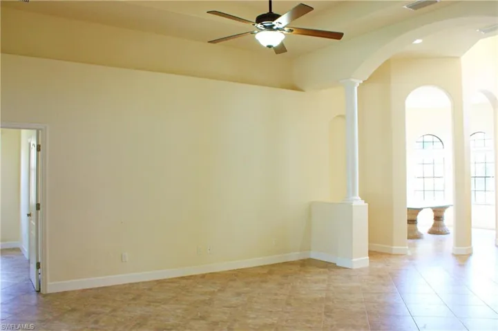 Living room with arched walkways, a ceiling fan, ornate columns, and light tile patterned floors