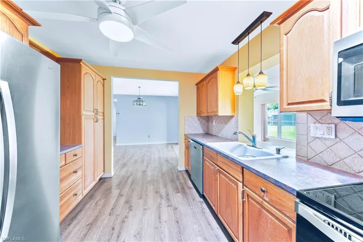 Kitchen with light hardwood / wood-style flooring, tasteful backsplash, hanging light fixtures, stainless steel appliances, and ceiling fan
