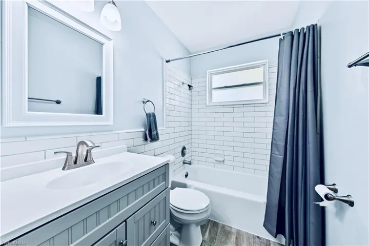 Full bathroom with hardwood / wood-style flooring, toilet, shower / bath combo with shower curtain, decorative backsplash, and vanity