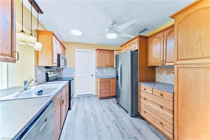 Kitchen with decorative light fixtures, backsplash, stainless steel appliances, ceiling fan, and light wood-type flooring