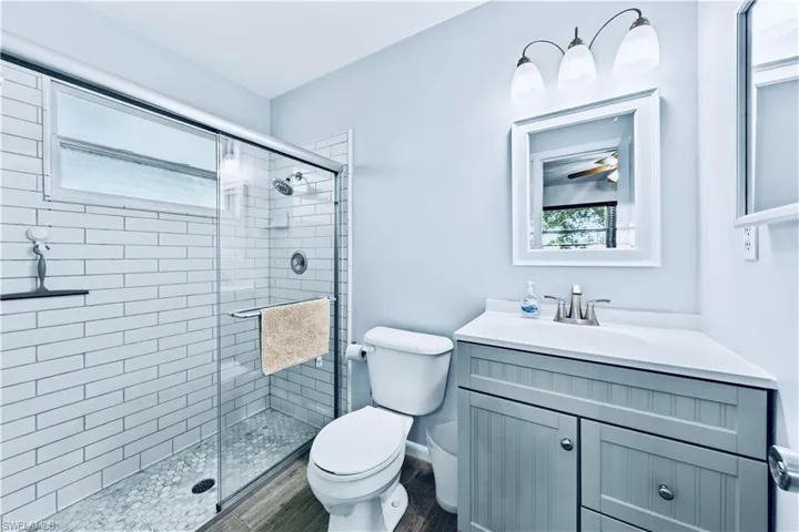 Bathroom featuring vanity, toilet, ceiling fan, and a shower with shower door