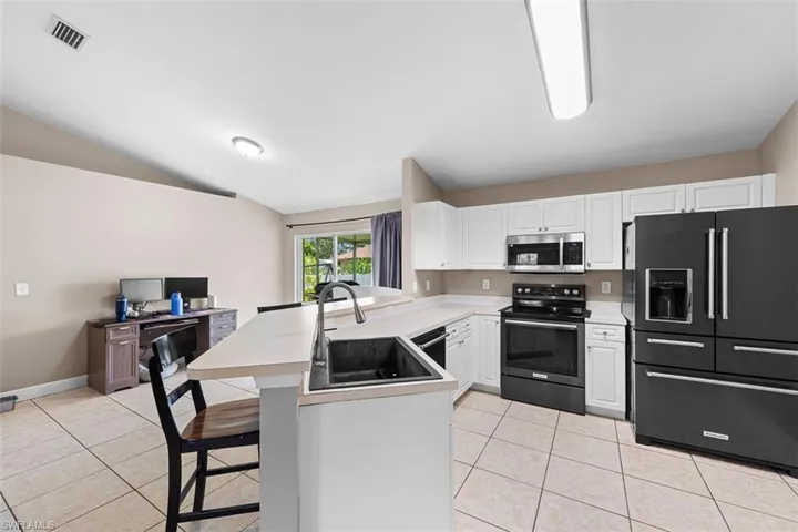 Kitchen featuring a kitchen breakfast bar, a peninsula, black appliances, light tile patterned flooring, and vaulted ceiling