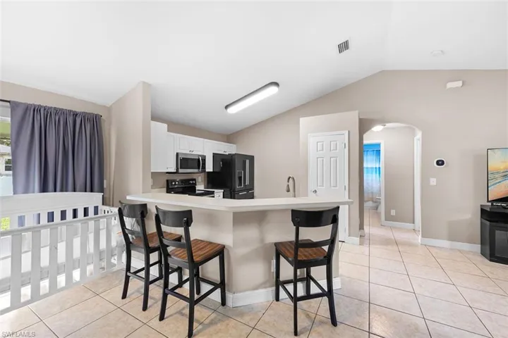 Kitchen with a kitchen breakfast bar, vaulted ceiling, light countertops, arched walkways, and a peninsula