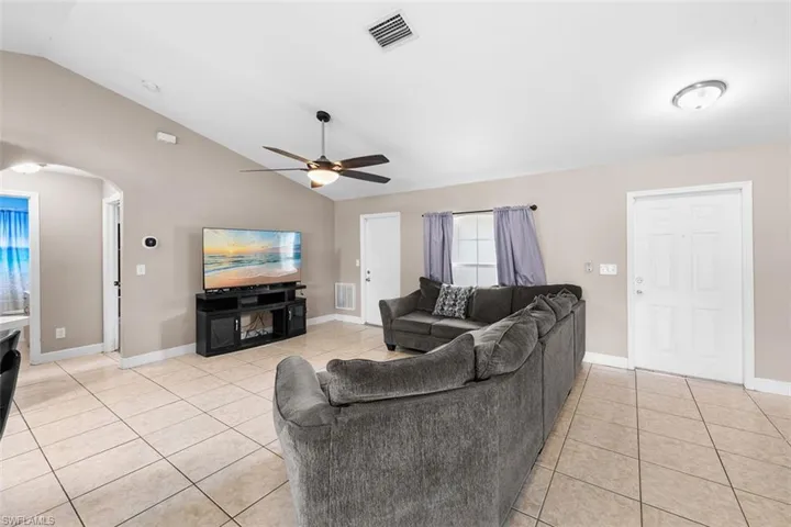 Living area featuring light tile patterned floors, arched walkways, a ceiling fan, and high vaulted ceiling