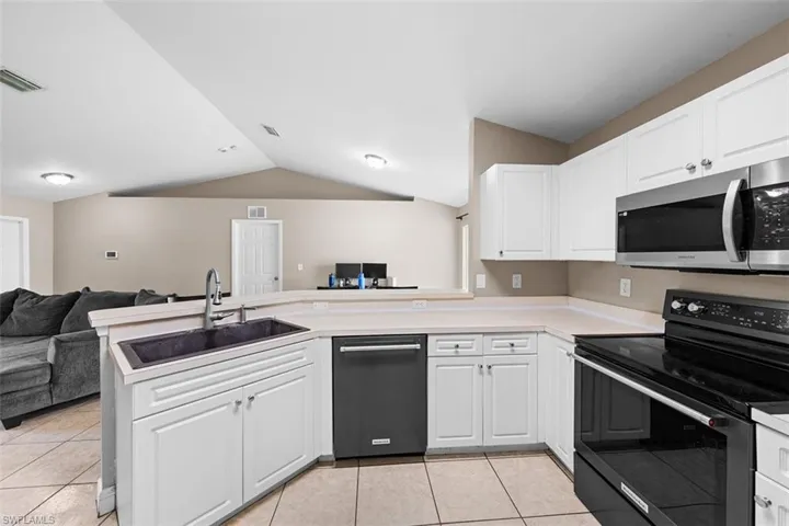 Kitchen featuring open floor plan, electric stove, stainless steel microwave, white cabinetry, and light tile patterned flooring