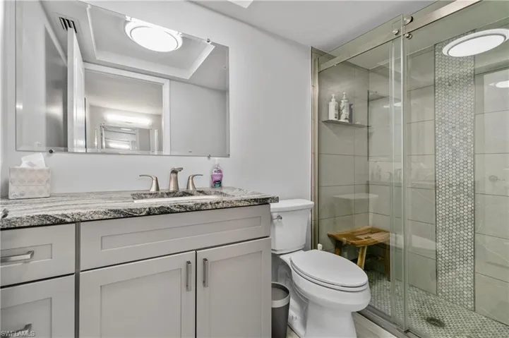 The MASTER BATHROOM features an ELEGANT STAND-UP SHOWER w/ INTRICATE TILE WORK, a stylish sliding shower door with chrome finishes & granite countertop w/ soft-close and light-gray cabinetry.