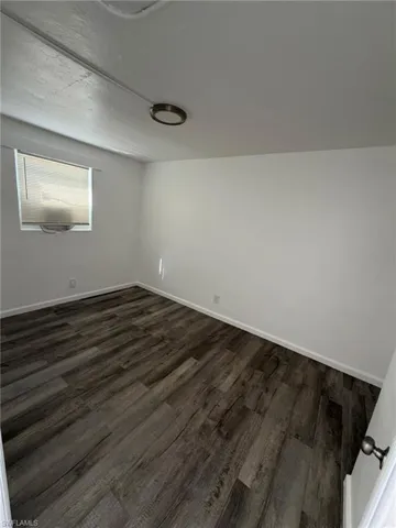 Spare room with dark wood-type flooring and baseboards