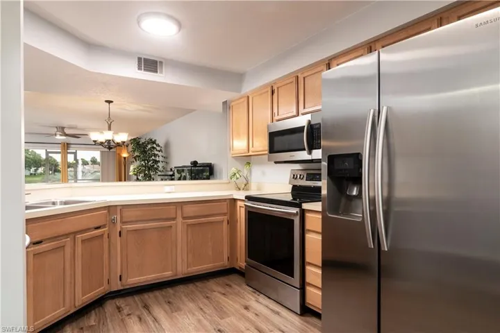 Kitchen with appliances with stainless steel finishes, light wood-style flooring, a chandelier, light countertops, and decorative light fixtures