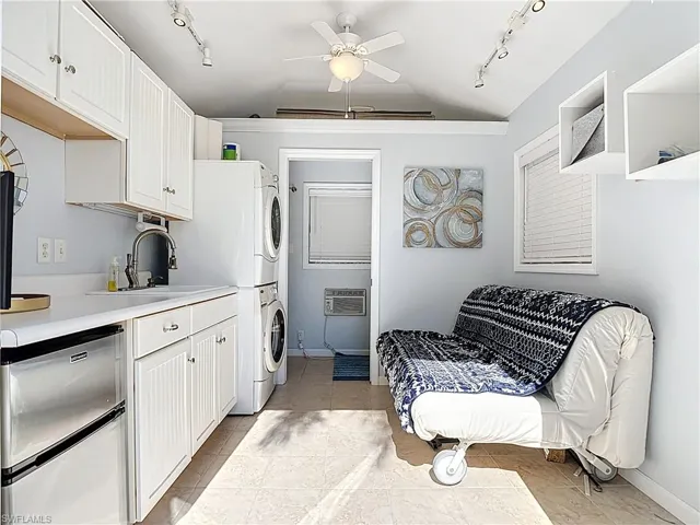 Kitchen with track lighting, white cabinetry, light countertops, vaulted ceiling, and stacked washing machine and dryer