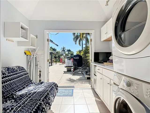 Washroom featuring cabinet space, stacked washer / dryer, light tile patterned flooring, and vaulted ceiling
