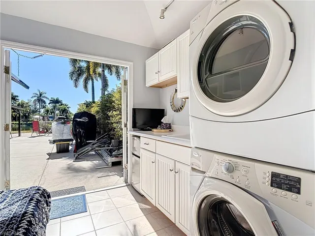 Laundry room with cabinet space, stacked washing machine and dryer, vaulted ceiling, and light tile patterned flooring