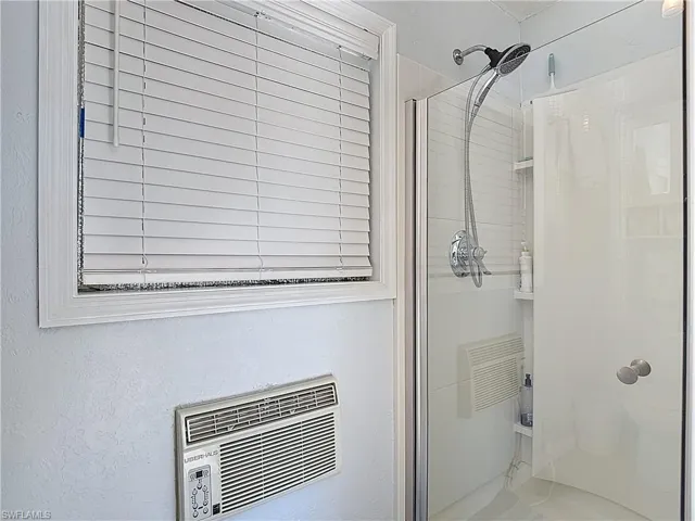 Full bath featuring a shower stall, a wall mounted AC, and a textured wall